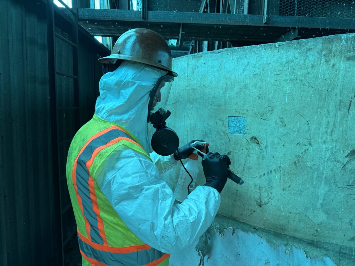 A man in white jacket and hard hat working on wall.