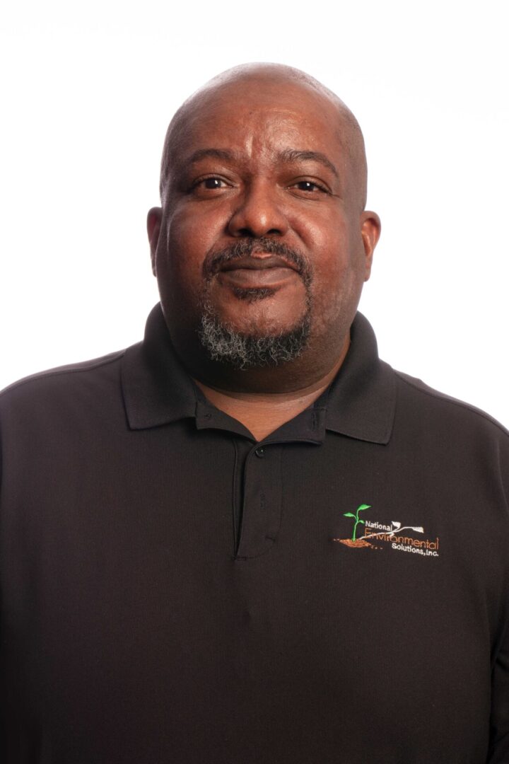 A man in black shirt standing next to white wall.